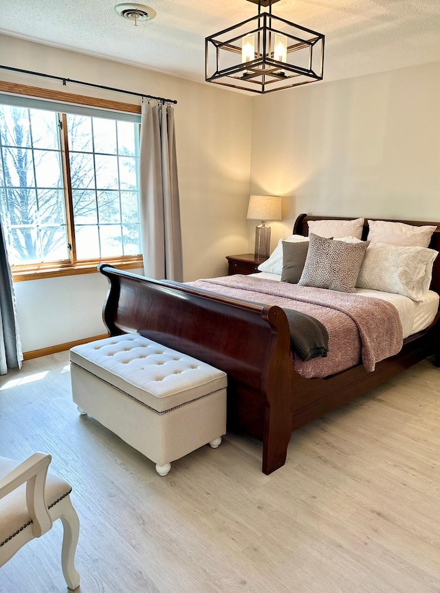 bedroom with light wood-type flooring, a chandelier, and a textured ceiling