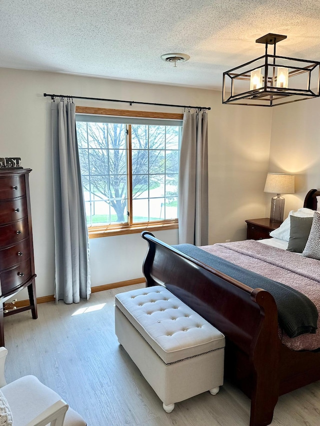 bedroom with a chandelier, light wood finished floors, baseboards, and a textured ceiling