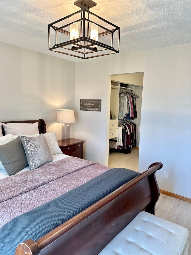 bedroom featuring a chandelier, a closet, light wood-style flooring, and a textured ceiling