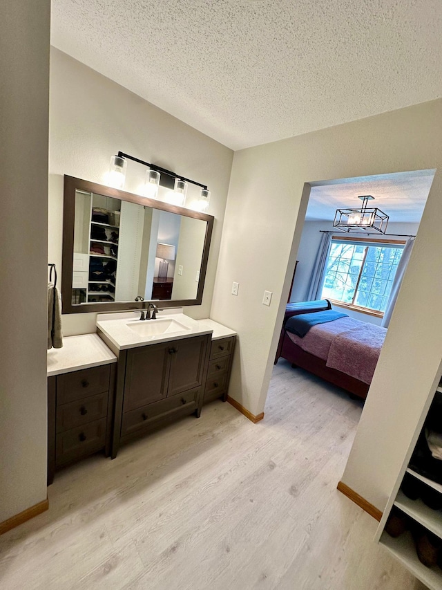 bathroom featuring a textured ceiling, wood finished floors, ensuite bath, vanity, and baseboards