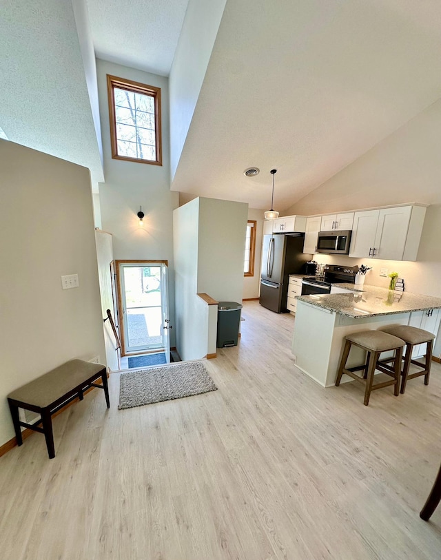 kitchen with stainless steel appliances, white cabinets, light wood finished floors, plenty of natural light, and high vaulted ceiling