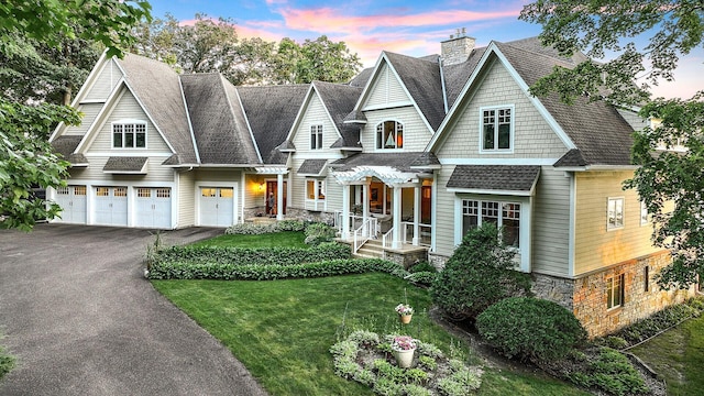 shingle-style home featuring stone siding, driveway, a chimney, and a garage