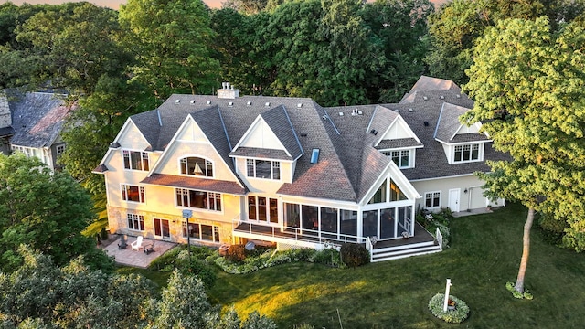 rear view of house with a sunroom, a patio, a lawn, and a chimney