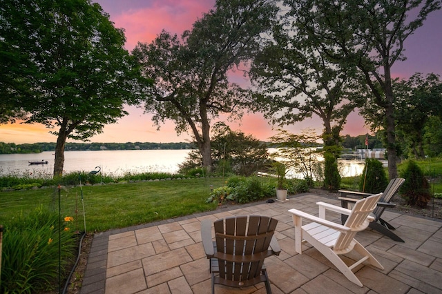 patio terrace at dusk with a water view and a lawn