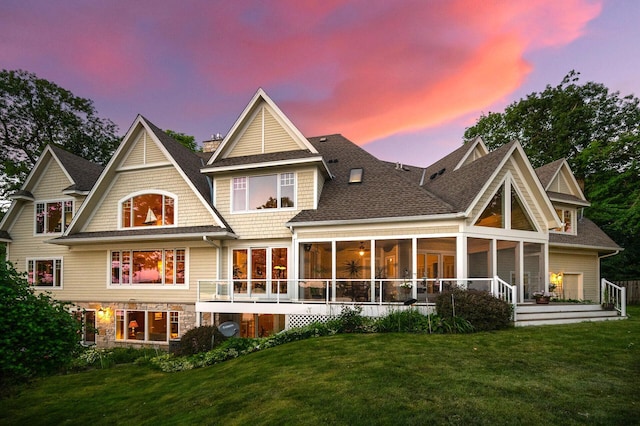 back of house featuring a lawn, roof with shingles, and a sunroom