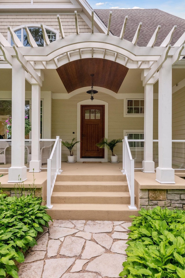 entrance to property with covered porch, a shingled roof, and a pergola