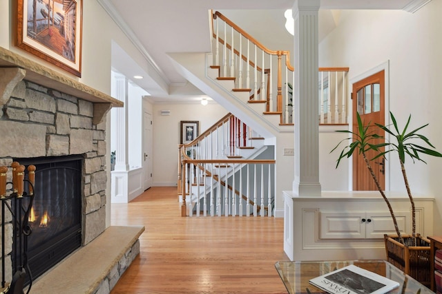 stairway with decorative columns, wood finished floors, ornamental molding, a stone fireplace, and baseboards