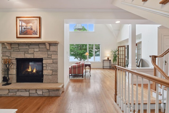 living area featuring wood finished floors, a stone fireplace, crown molding, baseboards, and stairway