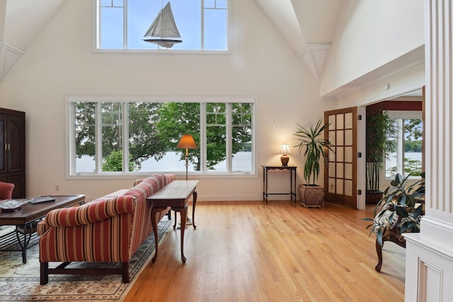 sitting room with high vaulted ceiling, healthy amount of natural light, light wood finished floors, and baseboards