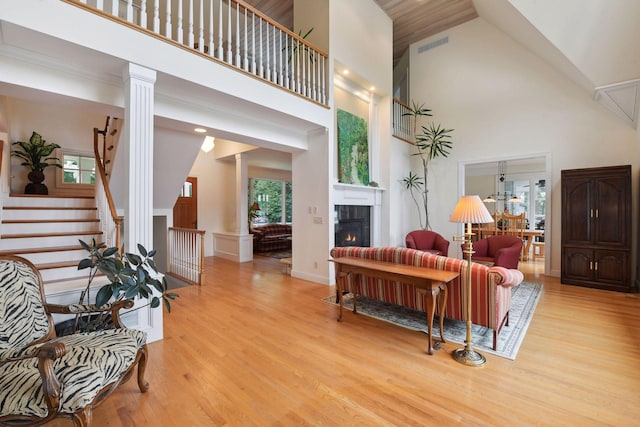 living area featuring a fireplace, wood finished floors, high vaulted ceiling, stairs, and ornate columns