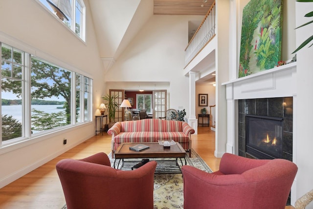 living room featuring plenty of natural light, a fireplace, light wood-type flooring, and a high ceiling