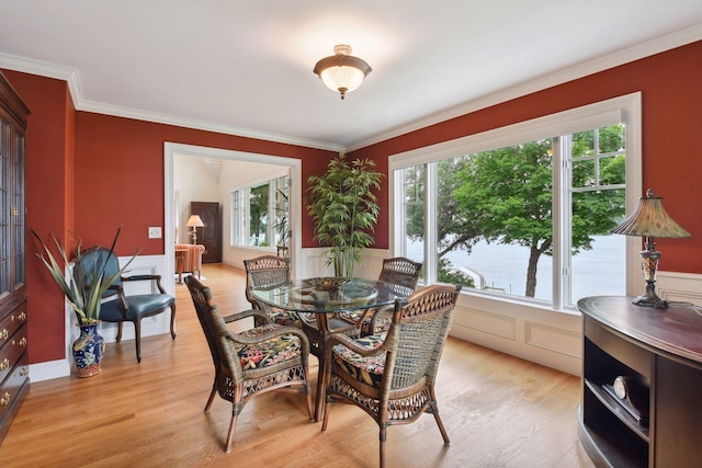 dining room with crown molding, light wood-style flooring, wainscoting, and a decorative wall