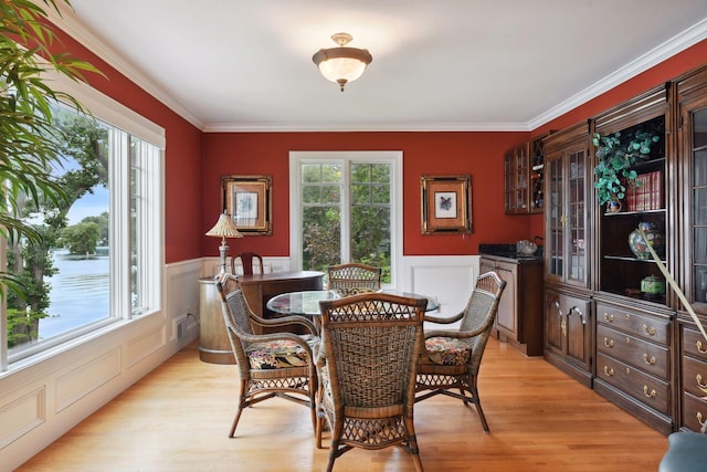 dining space with wainscoting, light wood-style flooring, and crown molding