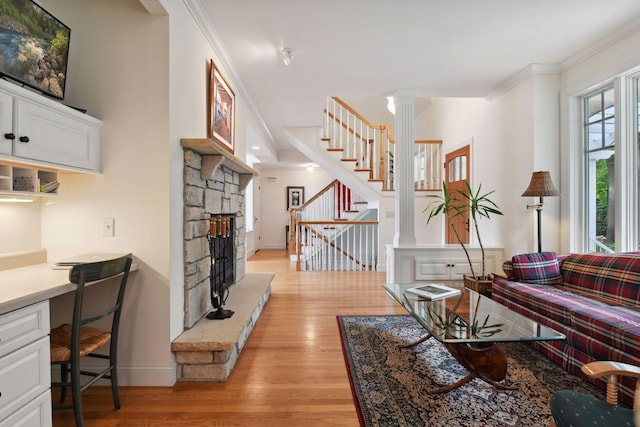 living room featuring a stone fireplace, decorative columns, light wood finished floors, stairs, and ornamental molding