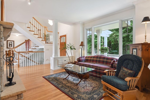 living room with ornate columns, wood finished floors, crown molding, and stairs