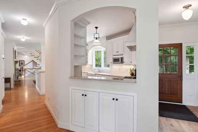 kitchen featuring stainless steel microwave, a sink, arched walkways, light wood finished floors, and crown molding