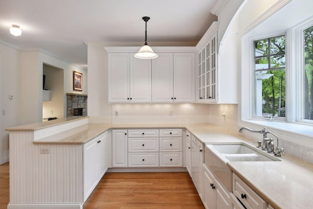 kitchen featuring a peninsula, white cabinetry, tasteful backsplash, glass insert cabinets, and light wood-type flooring