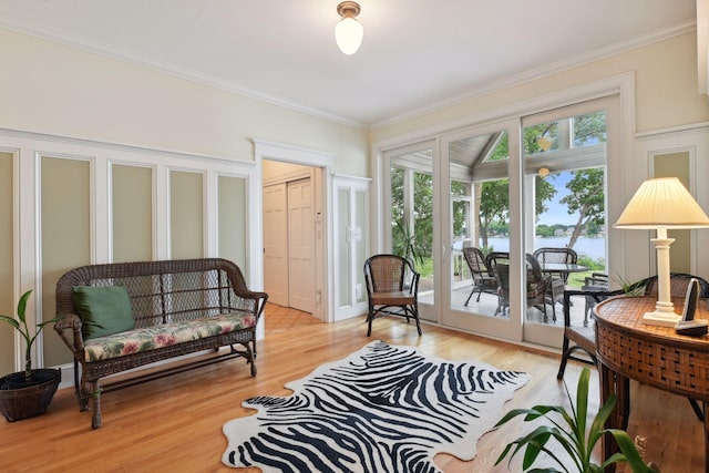 sitting room with plenty of natural light, ornamental molding, light wood-style floors, and a water view