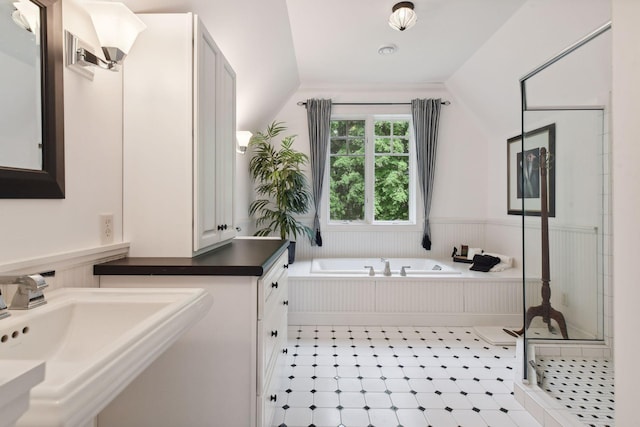 bathroom featuring lofted ceiling, a garden tub, a stall shower, a sink, and a wainscoted wall