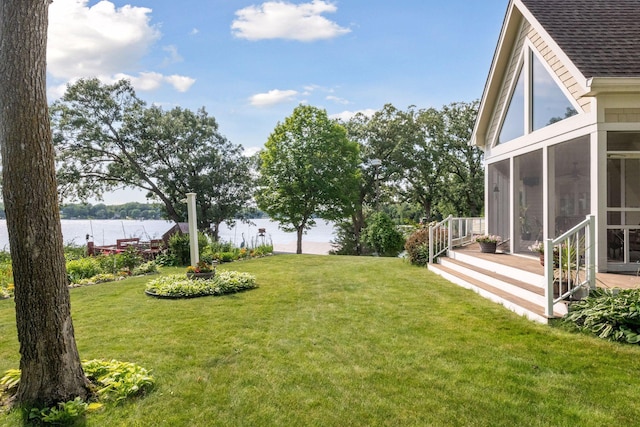 view of grassy yard featuring a sunroom and a water view