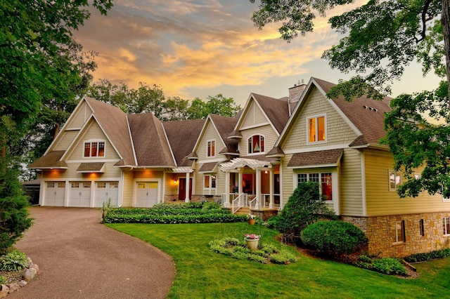 view of front facade featuring stone siding, a chimney, a lawn, driveway, and roof with shingles