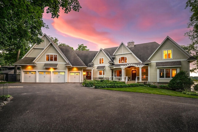 view of front facade with a porch, asphalt driveway, a chimney, an attached garage, and a shingled roof