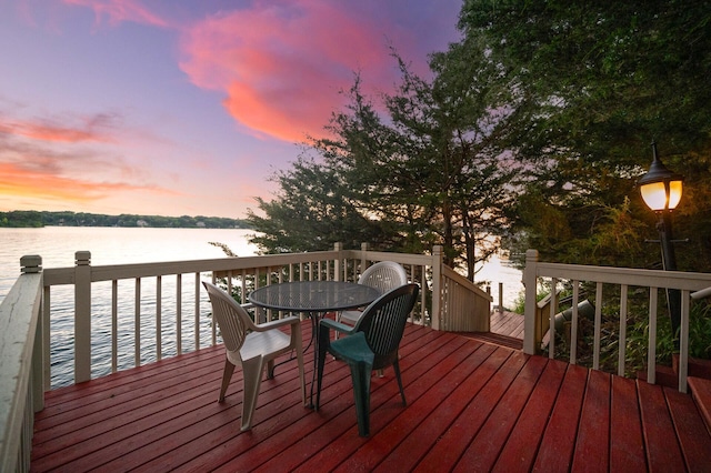 deck at dusk with a water view and outdoor dining space
