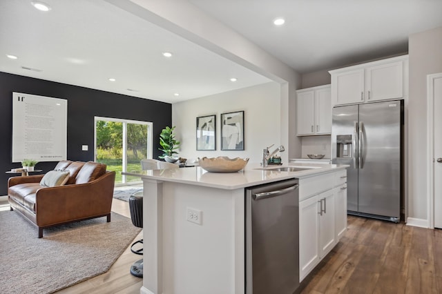 kitchen with appliances with stainless steel finishes, a sink, open floor plan, dark wood finished floors, and light countertops