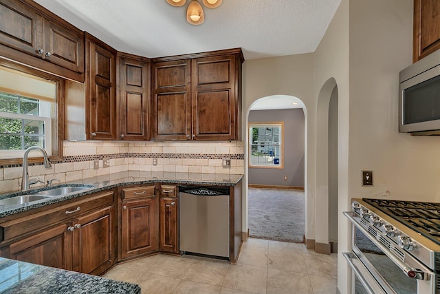 1317 8th Ave N, Saint Cloud, MN 56303 - kitchen featuring a sink, stainless steel appliances, arched walkways, dark stone counters, and decorative backsplash