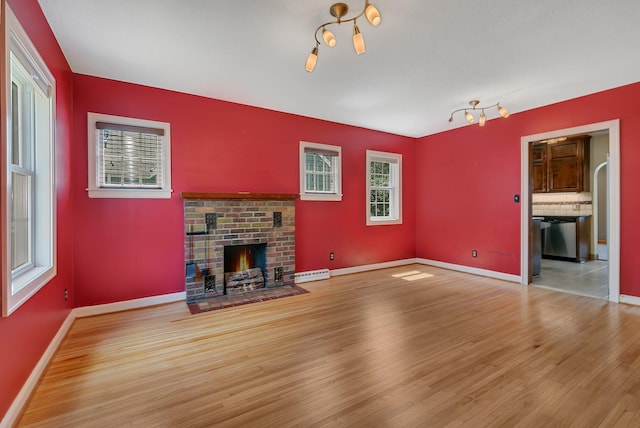 1317 8th Ave N, Saint Cloud, MN 56303 - unfurnished living room featuring wood finished floors, a brick fireplace, a baseboard radiator, and baseboards