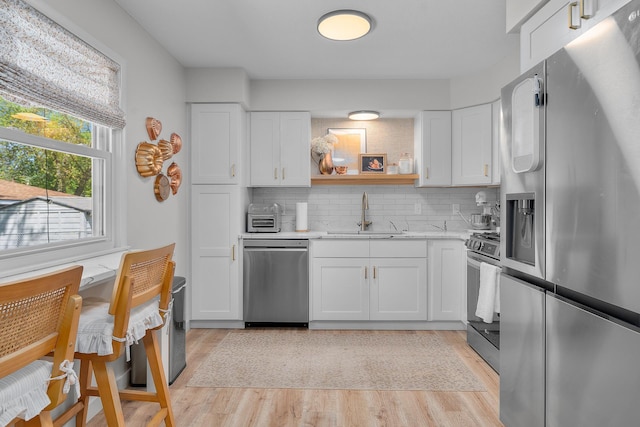 816 5th St S, Stillwater, MN 55082 - kitchen with appliances with stainless steel finishes, a sink, light wood finished floors, white cabinets, and decorative backsplash