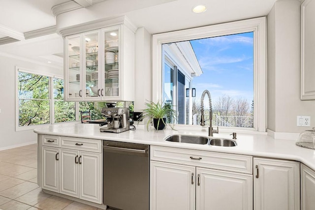 kitchen featuring stainless steel dishwasher, a sink, white cabinets, light countertops, and glass insert cabinets