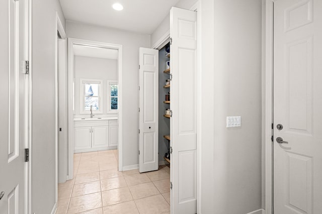 corridor with light tile patterned floors, baseboards, a sink, and recessed lighting