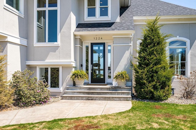 doorway to property featuring stucco siding and roof with shingles