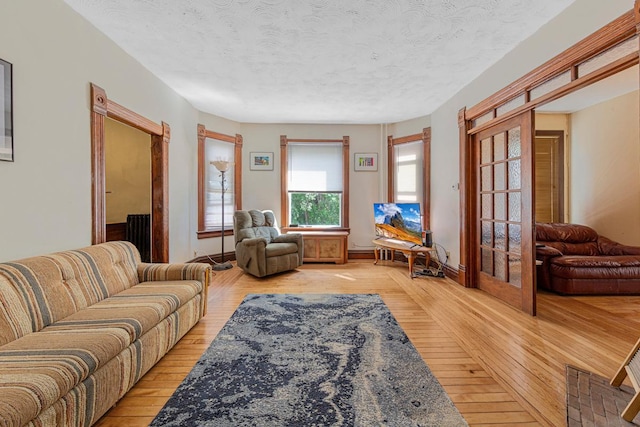 living room with light wood finished floors, a textured ceiling, baseboards, and french doors