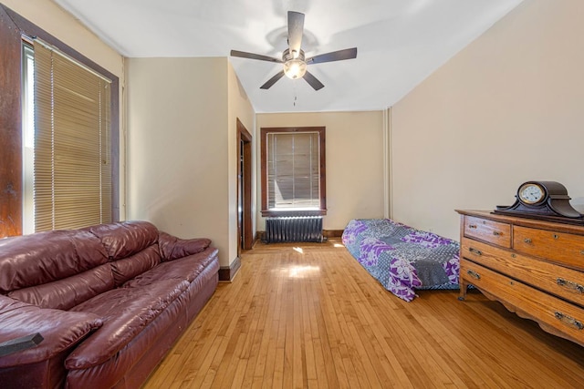 bedroom with radiator heating unit, light wood-type flooring, baseboards, and a ceiling fan