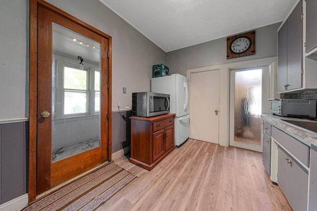 kitchen with stainless steel microwave, light wood-style flooring, freestanding refrigerator, and light countertops