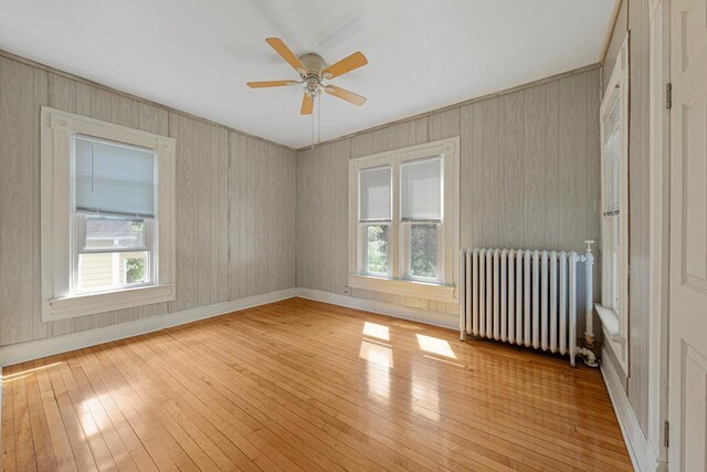 spare room with radiator, light wood finished floors, plenty of natural light, ceiling fan, and wooden walls