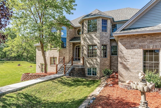 view of front of home with a front yard, brick siding, and a shingled roof