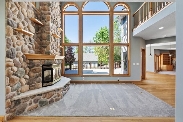 unfurnished living room with a stone fireplace, baseboards, wood finished floors, and a high ceiling
