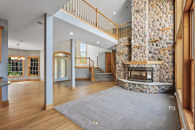 unfurnished living room featuring baseboards, wood finished floors, stairs, a stone fireplace, and a chandelier