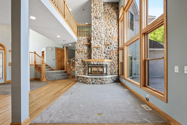unfurnished living room featuring wood finished floors, stairway, a fireplace, a towering ceiling, and baseboards