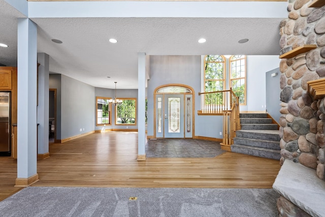 entrance foyer featuring a chandelier, wood finished floors, baseboards, stairway, and a textured ceiling