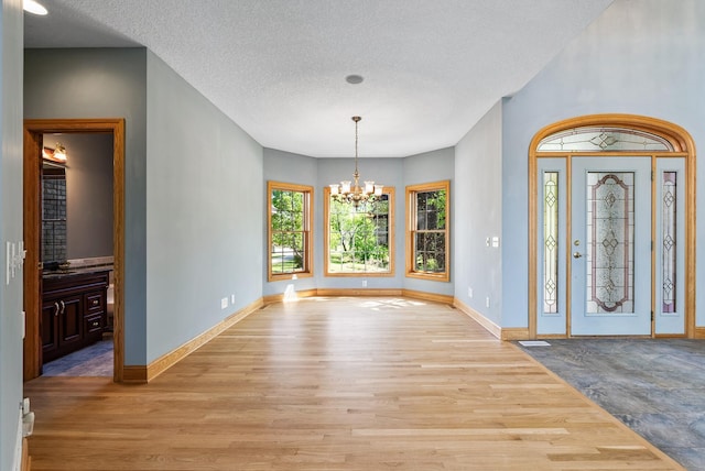 foyer with light wood finished floors, a chandelier, baseboards, and a textured ceiling