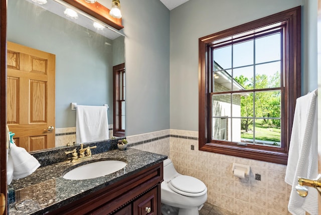 half bathroom with tile walls, wainscoting, toilet, vanity, and tile patterned flooring