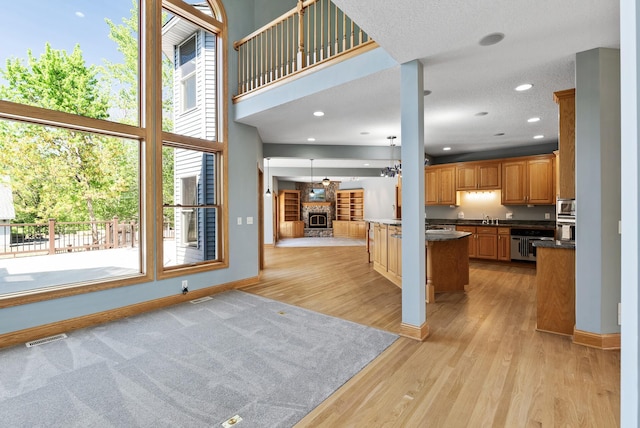 unfurnished living room featuring a fireplace with raised hearth, light wood-style flooring, baseboards, a sink, and recessed lighting