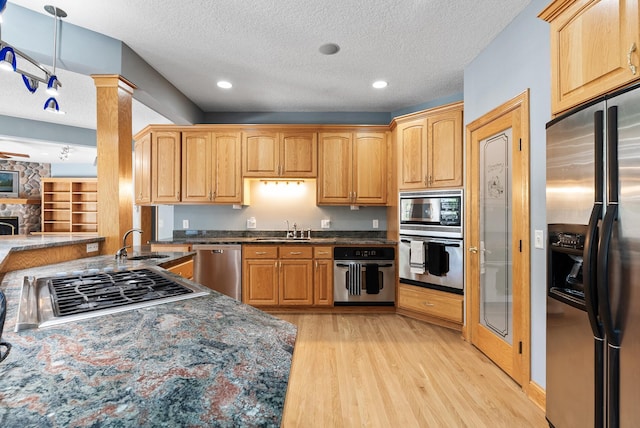 kitchen with appliances with stainless steel finishes, a sink, light wood finished floors, a textured ceiling, and dark stone counters