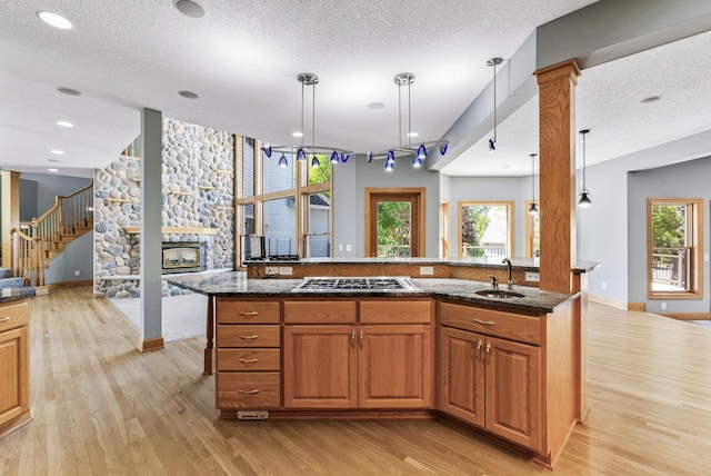 kitchen with stainless steel gas stovetop, a sink, light wood-type flooring, hanging light fixtures, and a textured ceiling
