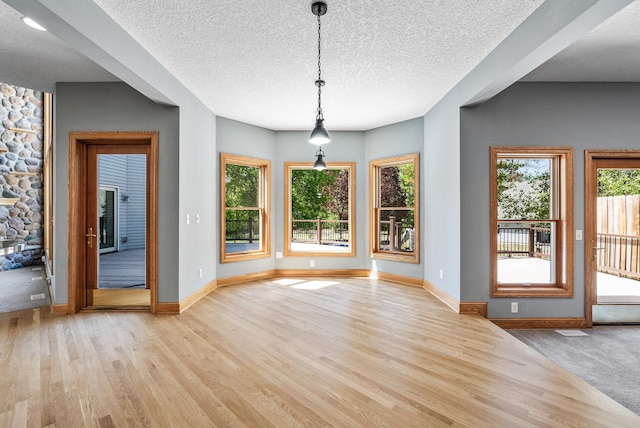unfurnished dining area featuring light wood-style floors, baseboards, and a textured ceiling