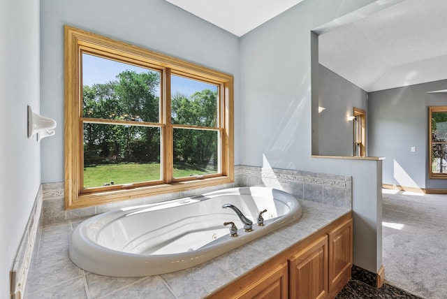 bathroom featuring healthy amount of natural light, a jetted tub, and vaulted ceiling